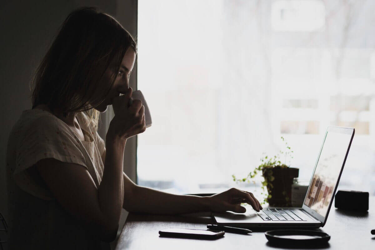 woman sipping out of a mug sitting at her desk looking at her computer