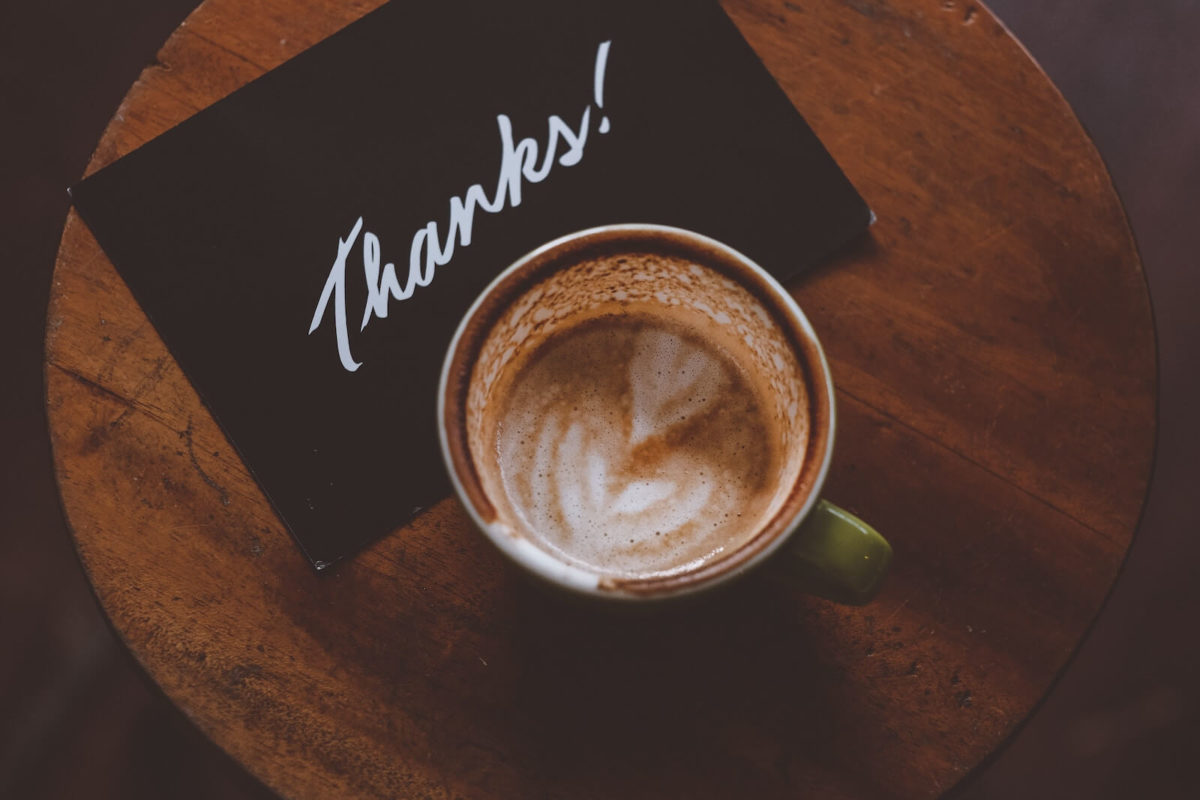 A coffee cup halfway full with remnants of latte art on a table with a folder that says Thanks