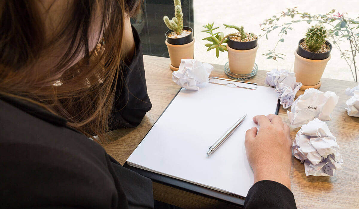 Person sitting at a desk with a notepad, five crumpled paper balls, and three succulent plants