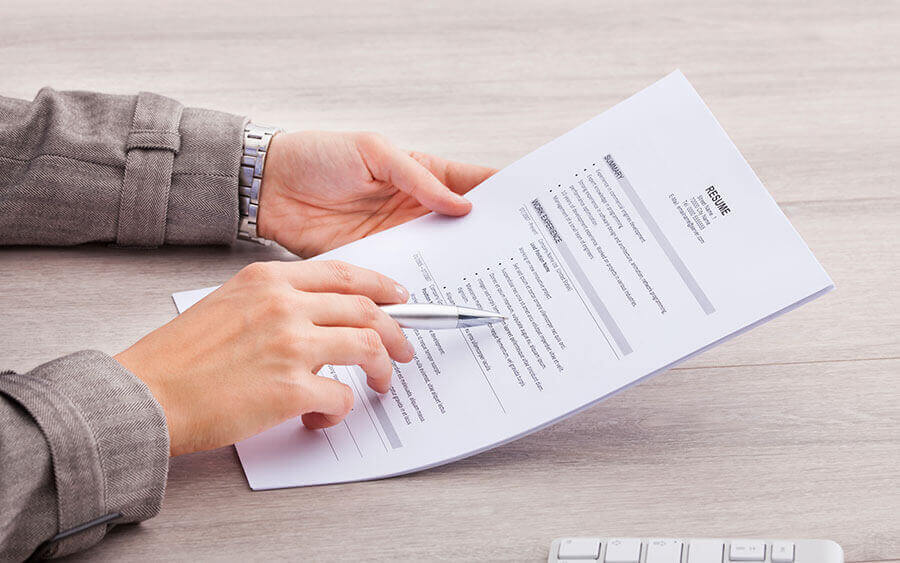 Two hands on a desk holding a resume near a computer keyboard