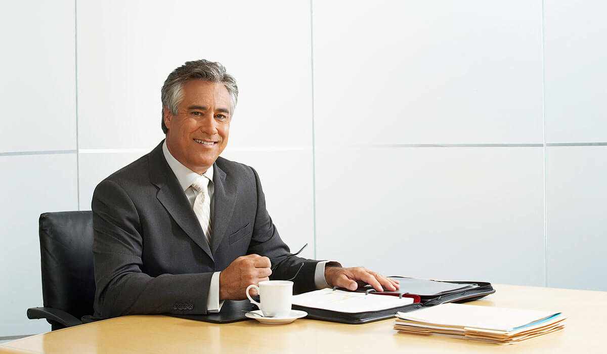 Business professional sitting at a table with a folder, stack of papers, and a cup of coffee