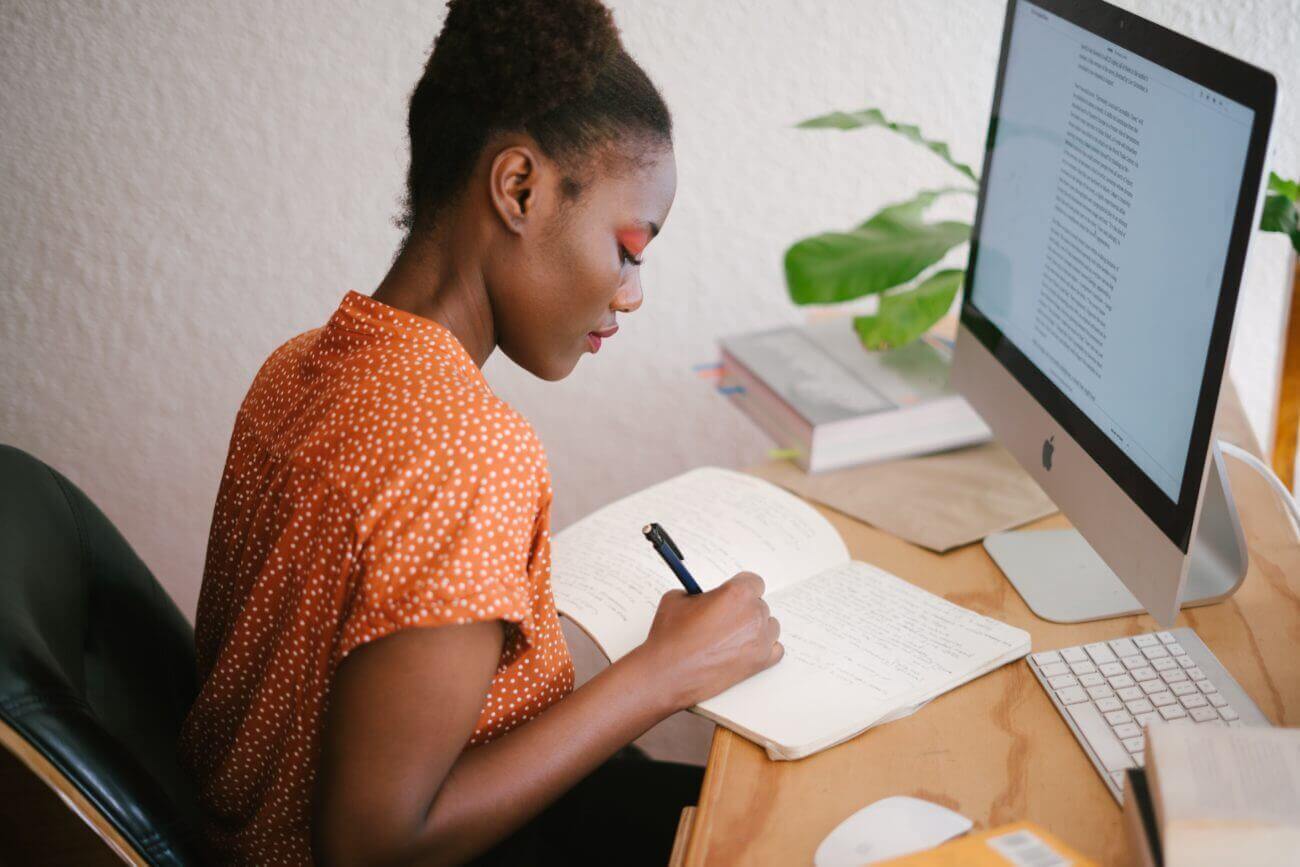 woman at a desk writing with a computer in front of her
