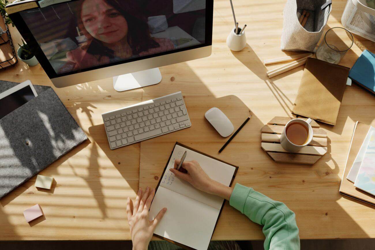tips-for-video-interviews writing at a desk with a video playing on the computer