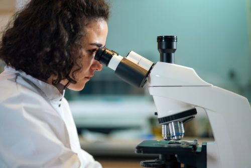 woman looking into a microscope while wearing a white lab coat