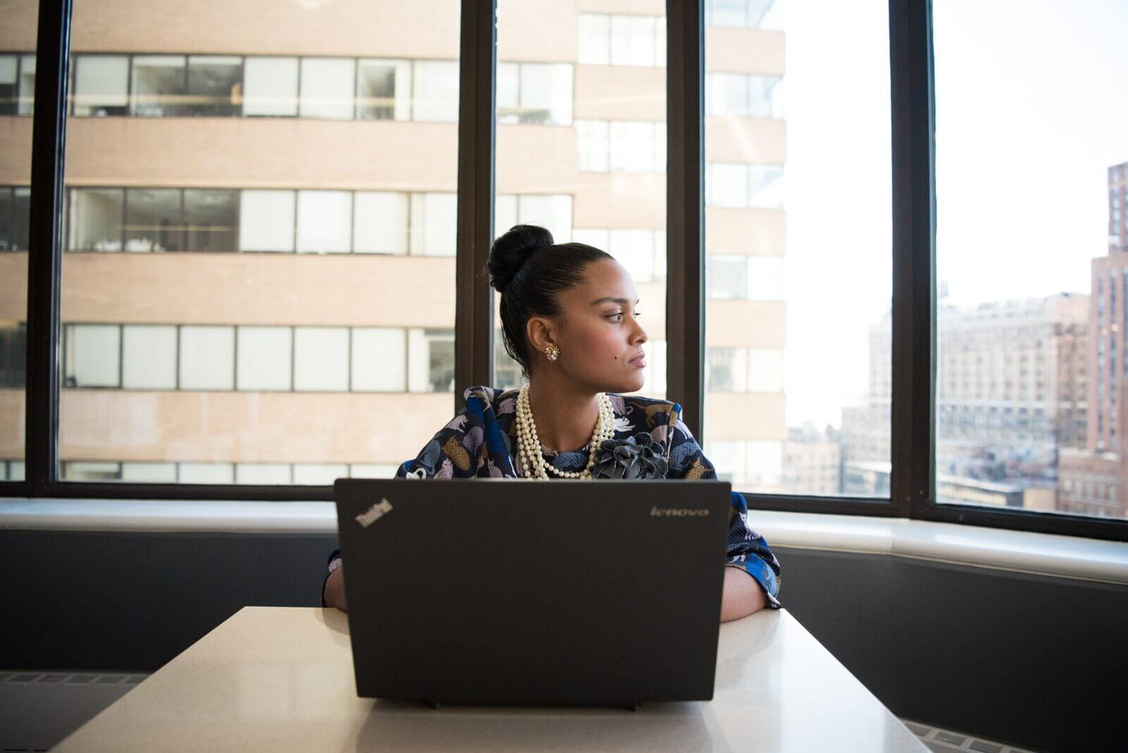woman sitting with her laptop staring outside a window thinking about her strengths and weaknesses at work
