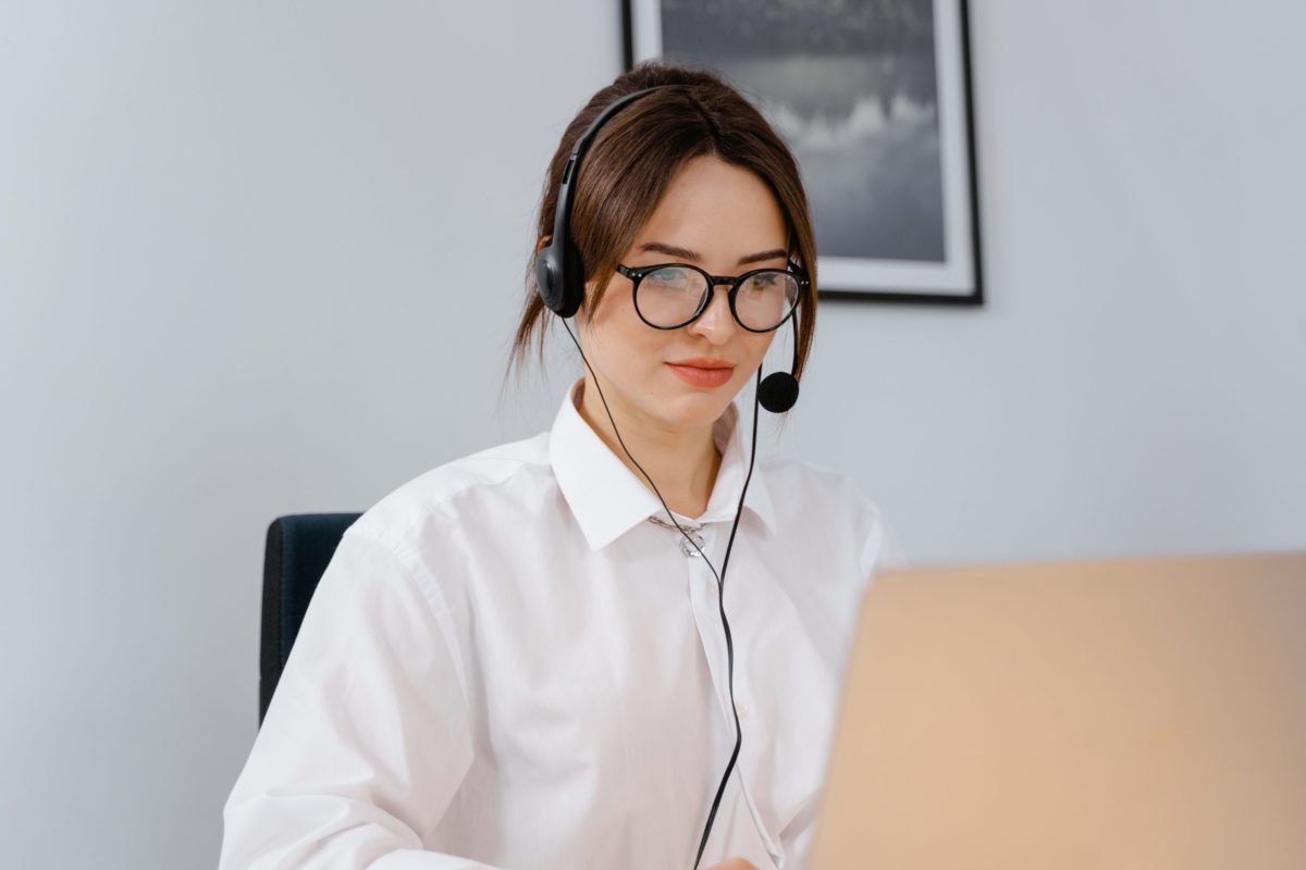 A remote work professional wearing a computer headset on sitting at a desk typing on a laptop