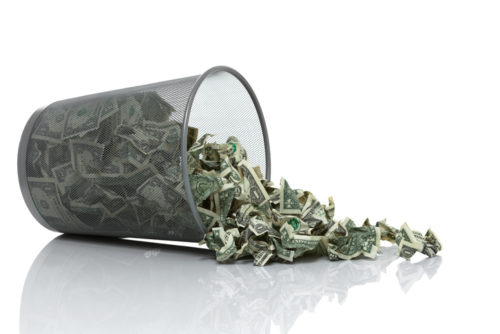 Metal wastebasket filled with crumbled money and tipped over