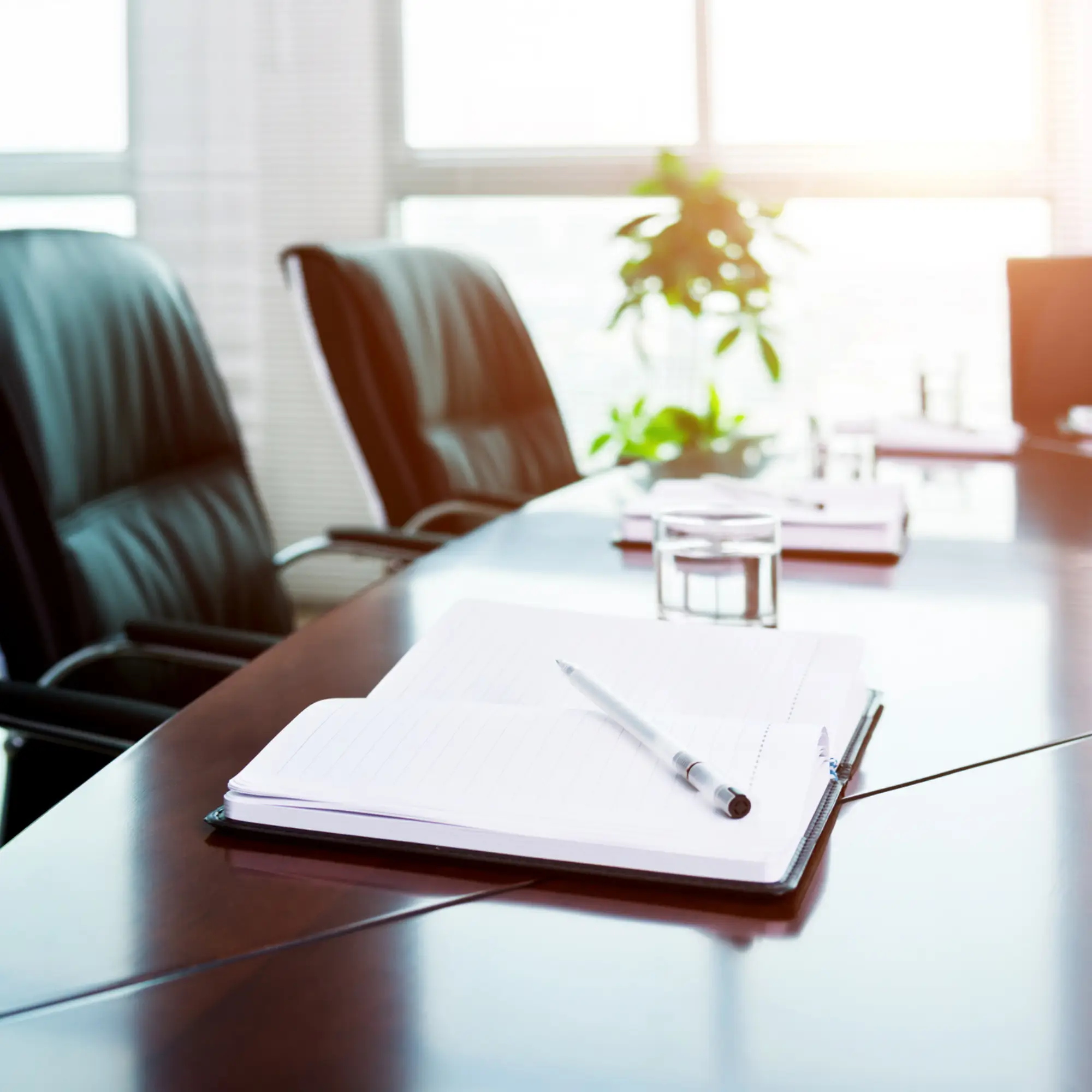 Board room with empty executive chairs and a notepad on the table.